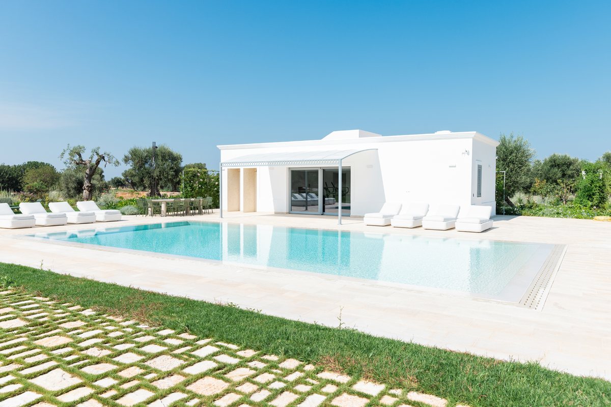Piscina rettangolare con bordo in pietra chiara davanti a una villa moderna