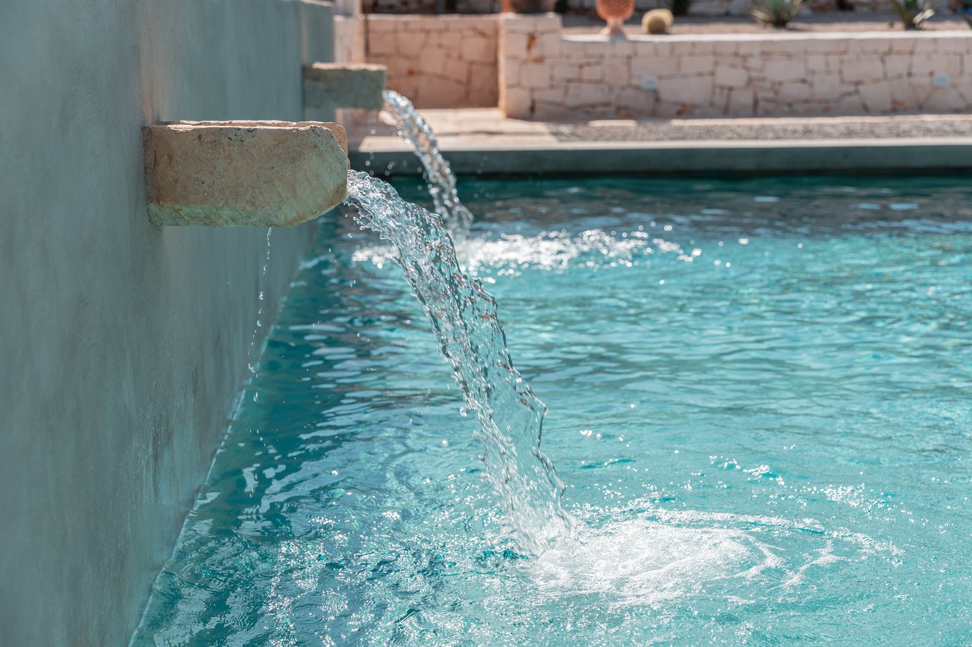 Piscina con muretto in pietra, pedana in legno e bocche a cascata